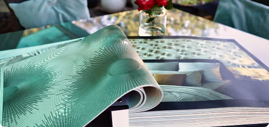 Ein teilweise aufgerolltes Magazin liegt auf einem Glastisch, im Hintergrund eine Vase mit roten Rosen.