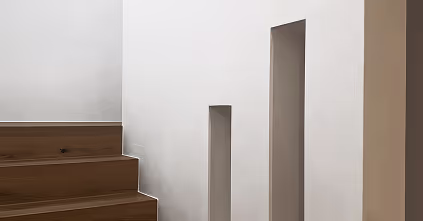 Minimalistische Treppe mit Holzstufen neben einer weißen Wand mit zwei rechteckigen Ausschnitten.