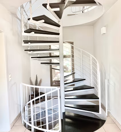 Moderne Wendeltreppe mit schwarzen Stufen und weißem Geländer in einem hellen Innenraum.