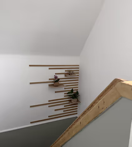 Treppenhaus mit weißen Wänden und Holzleisten, die horizontal an der Wand als Wanddeko angebracht sind, drei Pflanzenkübel sind an den Leisten befestigt.