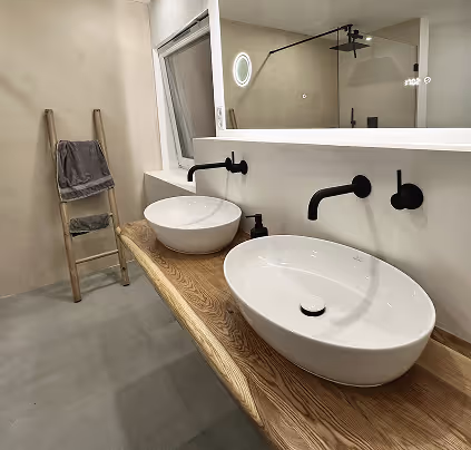 Modernes Badezimmer mit zwei weißen ovalen Waschbecken auf einer Holzplatte, schwarzen Wandarmaturen und einem großen Spiegel.