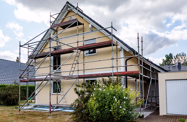 Ein Haus mit gelbem Putz ist von einem Gerüst umgeben, das für Bau- oder Renovierungsarbeiten aufgestellt ist.