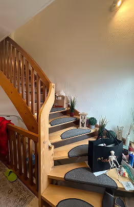 Holztreppe mit dunkelgrauen Treppenmatten, Pflanzen und Dekorationsartikeln an der Wand.