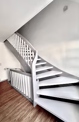 Weiße Wendeltreppe mit Holzstufen und weißem Geländer in einem modernen Innenraum mit Holzboden.
