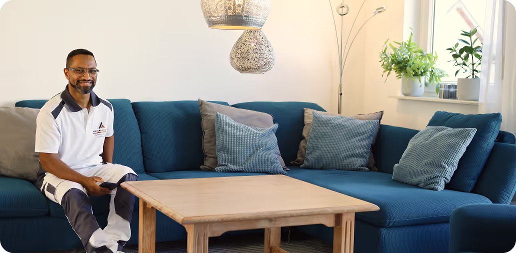 Mann in Arbeitskleidung sitzt auf blauem Sofa mit Kissen in modernem Wohnzimmer neben Holztisch.
